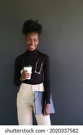 Portrait Of Smiling Female African Medical Student With Stethoscope, Folders And A Cup Of Coffee In A Black Background. Studio Shot.