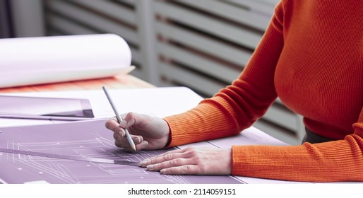 Portrait of smiling female architect drawing blueprints and plans while working at desk in office and looking at camera, copy space