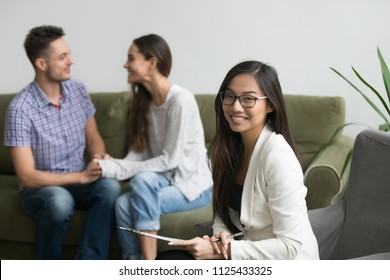 Portrait Of Smiling Female Asian Counselor With Happy Couple At Background, Professional Chinese Psychologist Looking At Camera, Marriage Counseling Therapy And Family Problems Solution Concept