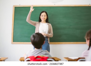 Portrait of Smiling female Asian teacher raising your hand and ask question to provide an example for students to answer in classroom. Motivated pupils, kids being engaged in learning process concept - Powered by Shutterstock