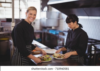 Portrait of smiling female chefs preparing fresh Greek salad at kitchen counter in cafe