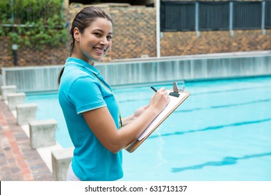 Portrait of smiling female coach writing on clipboard near poolside - Powered by Shutterstock