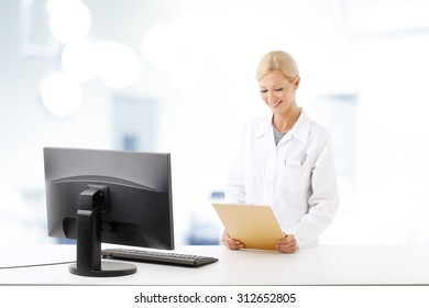Portrait of smiling female doctor standing at hospital. Healthcare worker holding hand clipboard and working on her computer.
