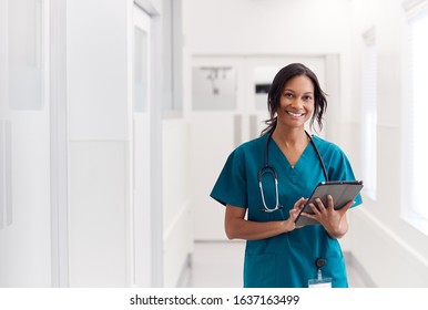 Portrait Of Smiling Female Doctor Wearing Scrubs In Hospital Corridor Holding Digital Tablet - Shutterstock ID 1637163499