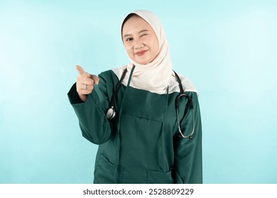 portrait of a smiling female doctor wearing green surgical while pointing forward and winking her eyes - Powered by Shutterstock