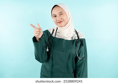 portrait of a smiling female doctor wearing green surgical while pointing forward and winking her eyes - Powered by Shutterstock