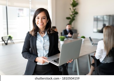 Retrato de una empresaria sonriente sosteniendo una laptop con equipo de fondo en la sala de conferencias de la oficina