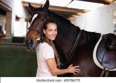 Portrait of smiling female jockey standing by horse in stable - Powered by Shutterstock