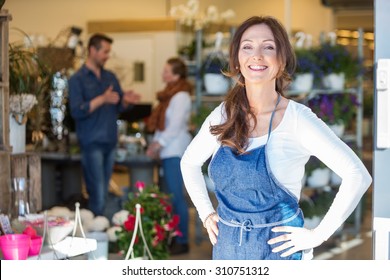 Portrait Of Smiling Female Owner With Customers In Background At Flower Shop