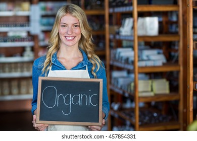 Portrait of smiling female staff holding a organic sign board in supermarket - Powered by Shutterstock