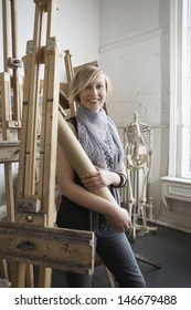 Portrait Of A Smiling Female Student Standing Amid Easels In Art College