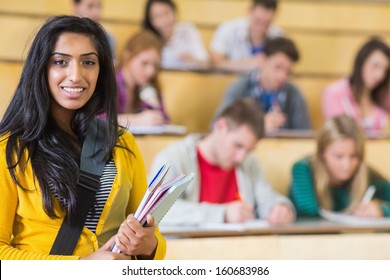 Portrait of a smiling female with students sitting at the college lecture hall