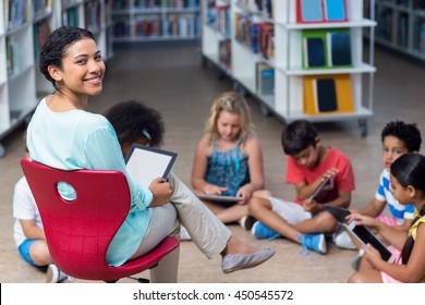 Portrait Of Smiling Female Teacher With Children Using Digital Tablets In Library