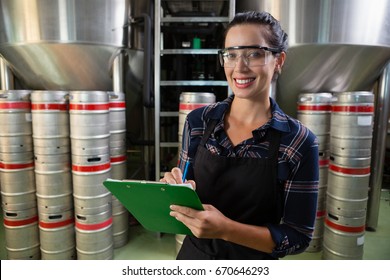 Portrait of smiling female worker holding clipboard by storage tanks at brewery - Powered by Shutterstock