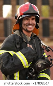 Portrait Of Smiling Fireman Wearing Fire Fighter Turnouts, Red Helmet And Breathing Apparatus, Closeup