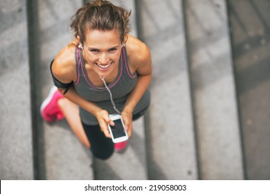Portrait of smiling fitness young woman with cell phone outdoors in the city