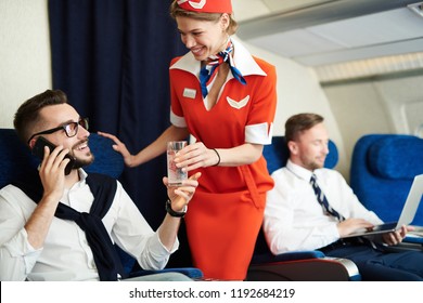 Portrait Of Smiling Flight Attendant Serving Glass Sparkling Water To Handsome Businessman Enjoying First Class Trip, Copy Space