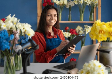 Portrait of smiling florist small business flower shop owner. Woman using her laptop and clipboard to take orders for her store. Copy space - Powered by Shutterstock