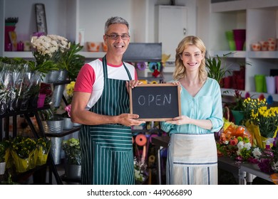 Portrait of smiling florists holding open sign on slate in flower shop - Powered by Shutterstock