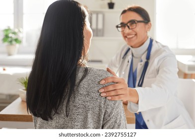 Portrait of smiling friendly doctor support female patient putting hand on her shoulder. Physician wearing stethoscope giving consultation a woman sitting back during medical examination in clinic. - Powered by Shutterstock