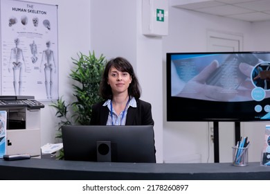 Portrait Of Smiling Front Desk Receptionist Waiting To Greet Patients In Private Practice Clinic Lobby. Professional Healthcare Worker Offering Support For Hospital Appointments.