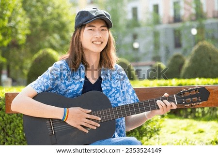 Portrait of a smiling gay man playing an acoustic guitar on a park
