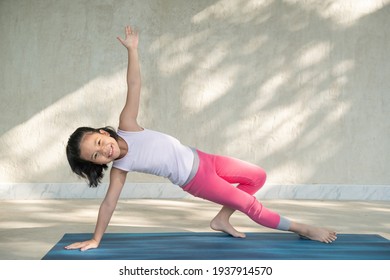 Portrait Of Smiling Girl Child Practicing Yoga, Standing In Vasisthasana Exercise, Side Plank Pose, Working Out Wearing Sportswear, Singlet, Pants, Indoor Full Length, White Studio Background.