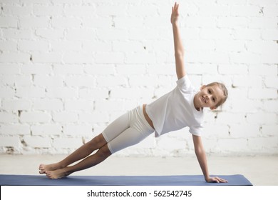 Portrait of smiling girl child practicing yoga, standing in Vasisthasana exercise, Side Plank pose, working out wearing sportswear, t-shirt, pants, indoor full length, white studio background  - Powered by Shutterstock