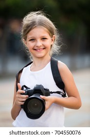 Portrait Of Smiling Girl In Elementary School Age Holding Photo Camera In Summer Day