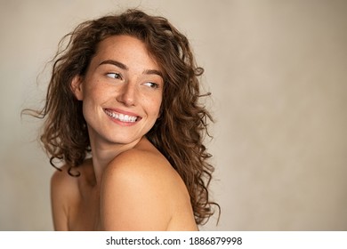Portrait of smiling girl enjoying beauty treatment on beige background. Beautiful natural woman looking at copy space, spa and wellness concept. Carefree laughing woman with bare shoulders isolated. 