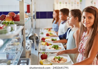 Portrait of smiling girl with food tray standing in line by friends during lunch break in school cafeteria - Powered by Shutterstock