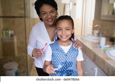 Portrait of smiling girl with grandmother holding toothbrushes in bathroom