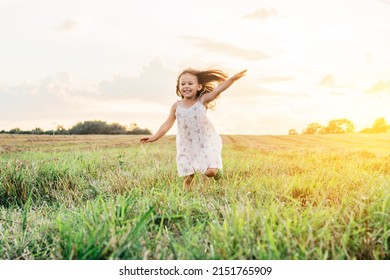 Portrait of smiling girl playing, jumping and running on grass hay field paths of dry grass in the sunset. Waving hands. Forest on bright light background. Cloudy sunny sky. Haying time - Shutterstock ID 2151765909