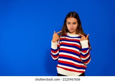 Portrait of smiling girl pointing at herself, bragging, rejoicing at winning, proud of achievement, wearing striped sweater. Indoor studio shot isolated on blue background - Shutterstock ID 2125967636