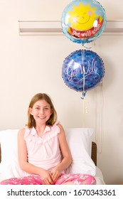 Portrait Of Smiling Girl Sitting In Hospital Bed With Get Well Balloons