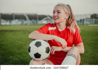 Portrait of smiling girl soccer player with ball sitting on the grass - Powered by Shutterstock