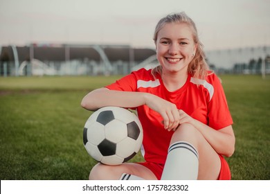 Portrait of smiling girl soccer player with ball sitting on the grass