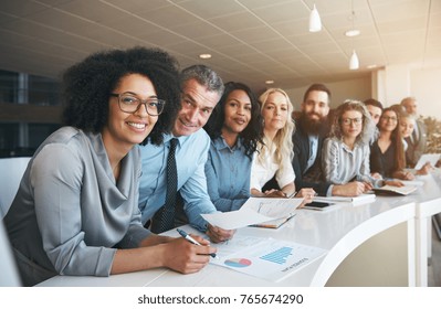 Portrait of a smiling group of diverse corporate colleagues standing in a row together at a table in a bright modern office - Shutterstock ID 765674290