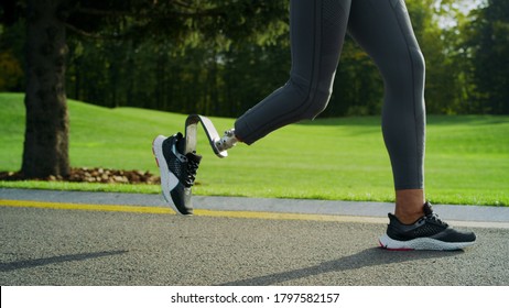 Portrait Of Smiling Handicapped Athlete Jogging On Road. Fitness Girl Running On In Park. Close Up Runner Woman Legs Training Outdoors In Slow Motion. Disabled Woman Running Outside