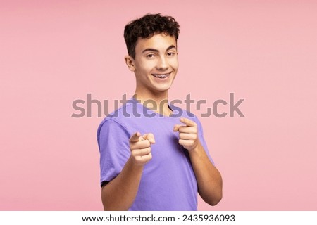 Portrait of smiling handsome boy wearing braces, pointing fingers, looking at camera. Attractive teenager wearing stylish clothes isolated on pink background. Shopping concept, advertisement