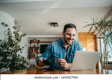 Portrait Of A Smiling Handsome Man Looking At Laptop At Home Office, Holding Eyeglasses And Cup Of Coffee.