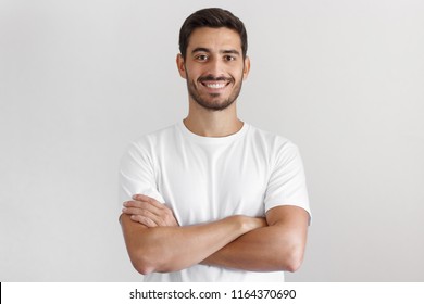 Portrait Of Smiling Handsome Man In White T-shirt, Standing With Crossed Arms Isolated On Gray Background