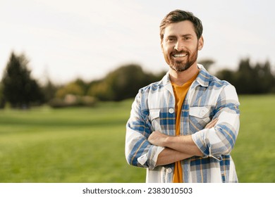 Portrait of smiling handsome middle aged man farmer wearing s stylish t shirt holding arms crossed looking at camera standing in green field, copy space. Successful business concept   - Shutterstock ID 2383010503