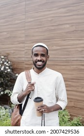 Portrait Of Smiling Handsome Young Islamic Student In Kufi Cap Standing With Satchel And Takeout Coffee Cup