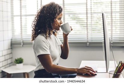 Portrait of smiling happy african american black woman relaxing using technology of desktop computer while sitting on table.Young creative african girl working and drink coffee at home.work from home