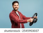 Portrait of smiling, happy bearded man holding steering wheel, looking at camera, posing isolated on blue background. Vehicle, transportation concept