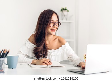 Retrato de sorrir feliz linda mulher asiática relaxante usando a tecnologia do computador portátil enquanto está sentado na mesa. Jovem garota criativa trabalhando e digitando no teclado em casa. trabalho em casa conceito