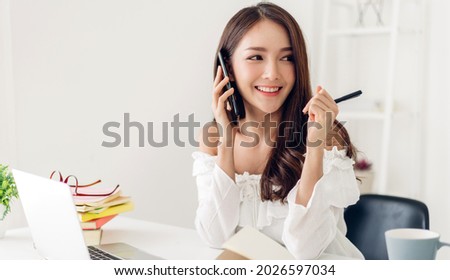 Portrait of smiling happy beautiful asian woman relaxing using technology of laptop computer while sitting on table.Young creative girl working and talk with smartphone at home.work at home concept