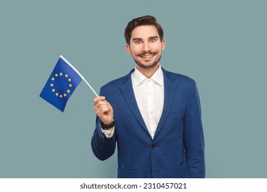 Portrait of smiling happy handsome man with mustache standing waving europe union flag, expressing happiness, wearing white shirt and jacket. Indoor studio shot isolated on light blue background. - Powered by Shutterstock