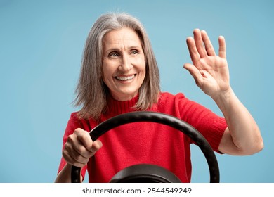 Portrait of smiling, happy mature woman, senior driver holding steering wheel waving hand, looking away, isolated on blue background. Transportation concept - Powered by Shutterstock